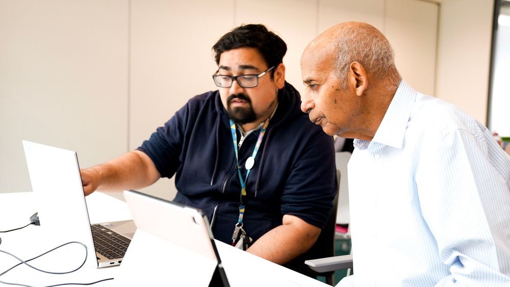 Two people using tablets and laptops together during a library digital skills session