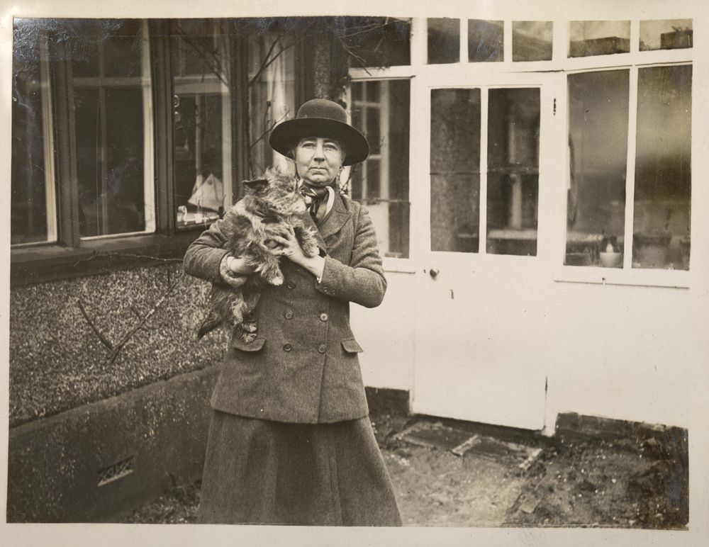 Sepia photo of Frances Wolseley in a hat with a small dog in front of a house.