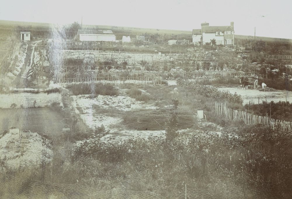 Sepia aerial photo of a terraced landscape with fields and a large house on a hill. A small shed and horse and cart are visible.