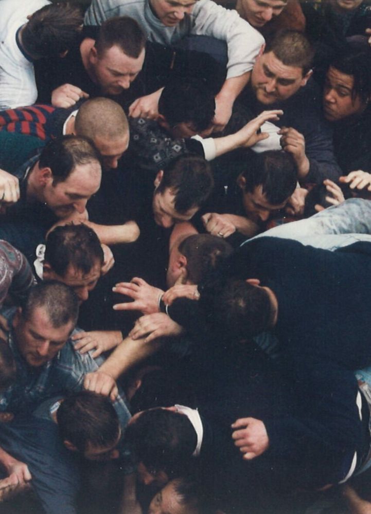 Crowd of people in a mass scrum, wrestling over an unseen ball