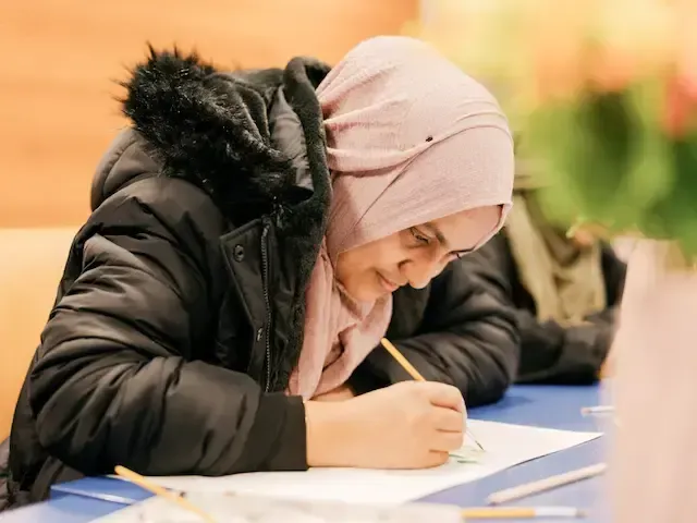 A woman in a pink headscarf writing by hand