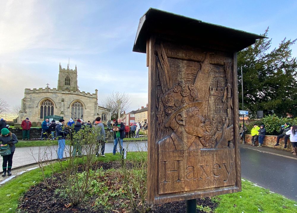 A wooden sign depicting the Haxey Hood. A church in the background.