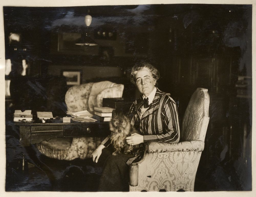 A woman in an armchair with a small dog on her lap.