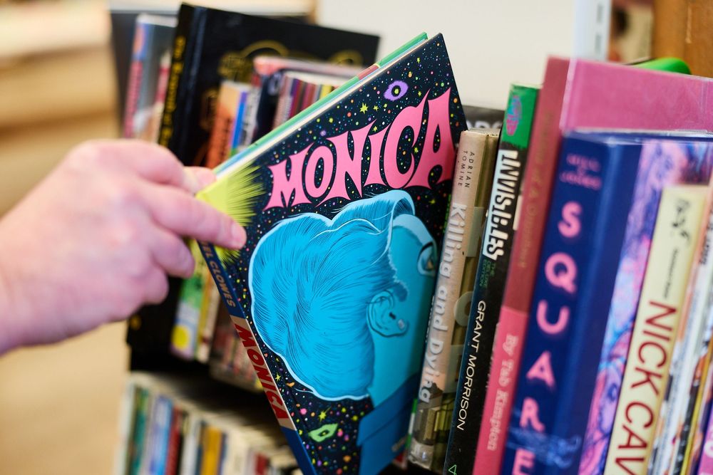 A close-up of a person's hand removing a book entitled 'Monica' from a shelf full of books.
