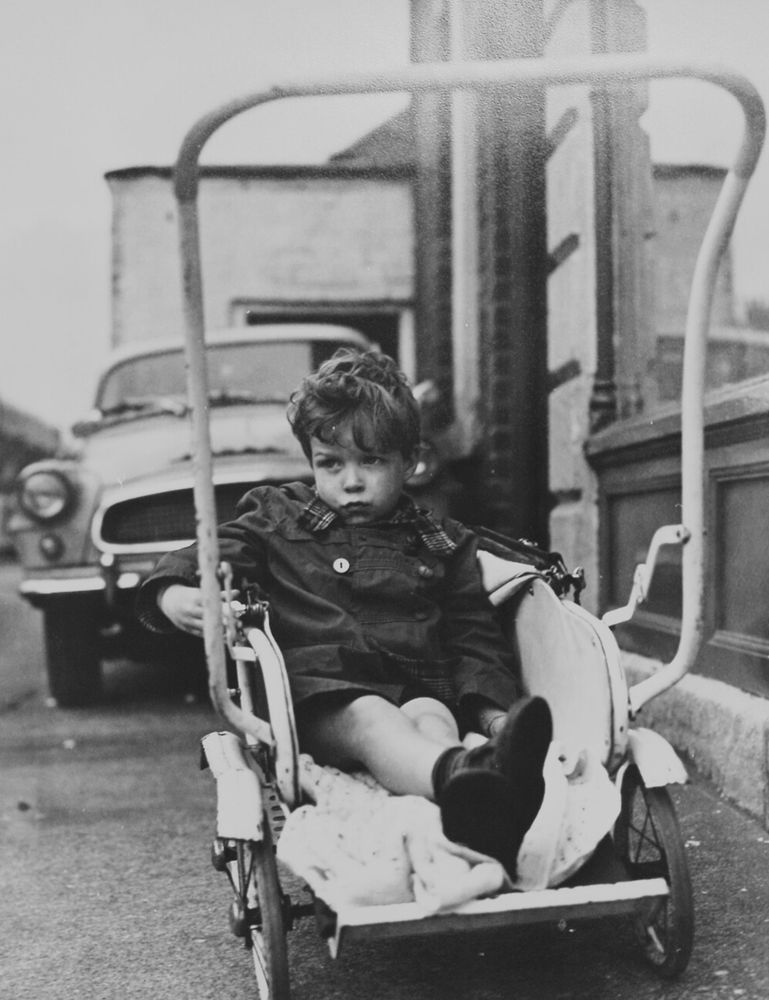 A black & white photo of a young boy in shorts reclining in a buggy.