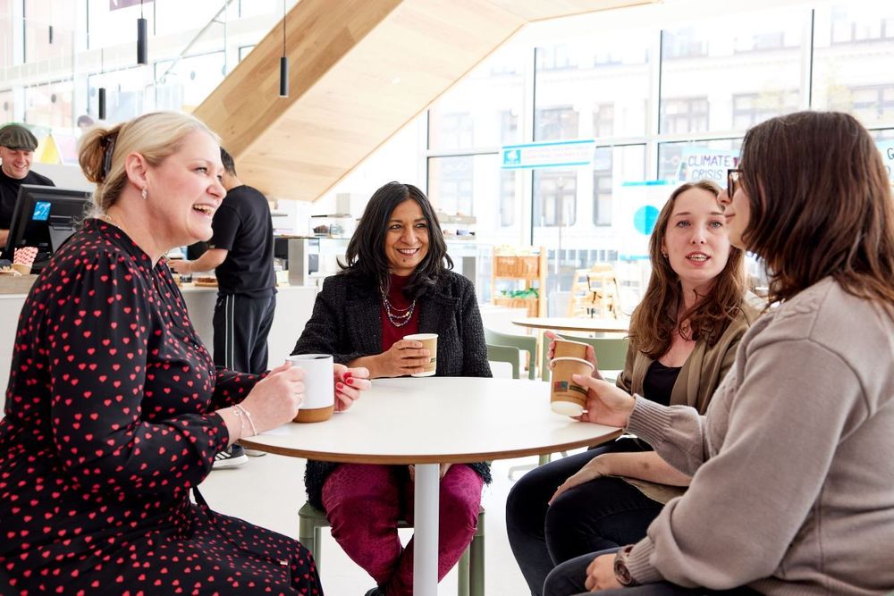 A group of people chat as they sit around a table in a library cafe.