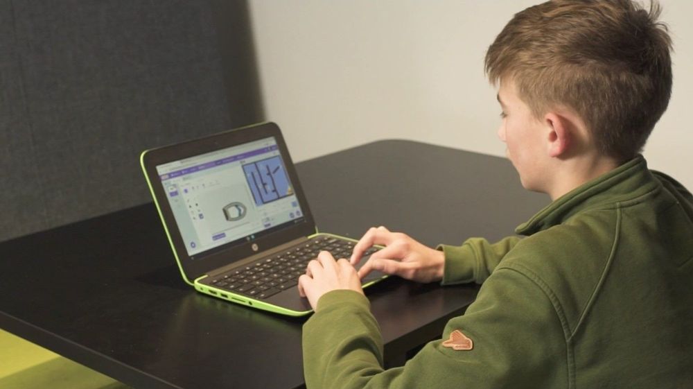 A teenage boy coding on a laptop in a library.